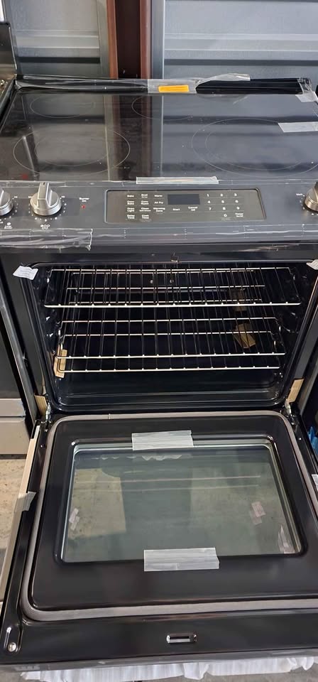 A black built-in range hood and oven combo with the oven door open, showing the interior racks and glass door. The top section has a glass cooktop with control knobs and a digital display on the front.