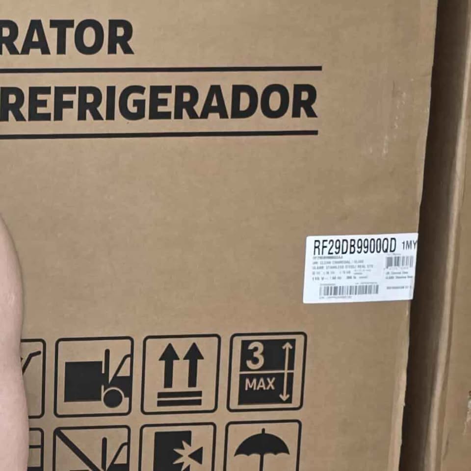 A close-up of a brown cardboard shipping box with black printed text reading 'REFRIGERADOR' and handling icons, plus a white product label sticker with a barcode and tracking number.