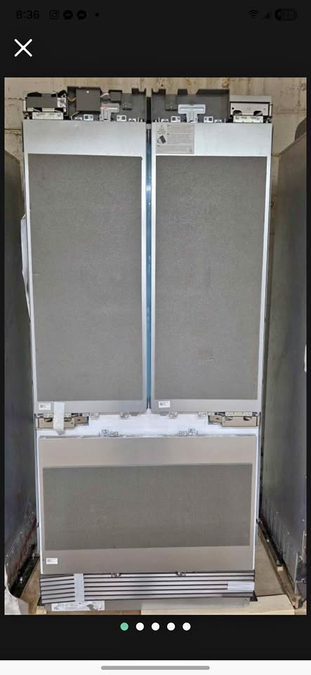 A front-loading double-door refrigerator shown from the back, with the doors open and the interior racks visible. The appliance has a silver metal exterior with gray interior panels and a black control panel at the top.