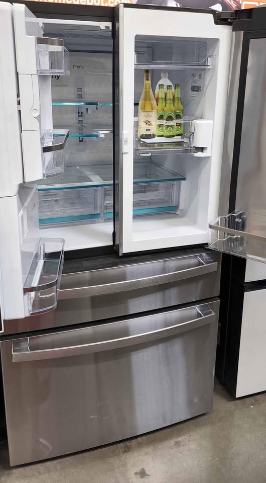 A stainless steel French door refrigerator with both doors open, showing the empty interior shelves and door bins. The lower freezer drawer is also open.