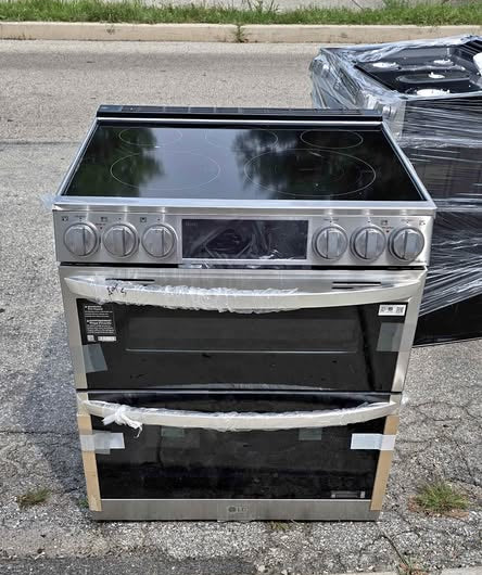 A stainless steel electric range LG 7.3 Cu Ft Smart Double Oven Electric Slide-In Range with InstaView with a black glass cooktop and two oven doors, sitting on a concrete surface outdoors.