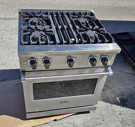 A stainless steel gas range, Viking Professional 5 Series 30" Freestanding Gas Range stove with black burners and control knobs, photographed outdoors on pavement next to a road.