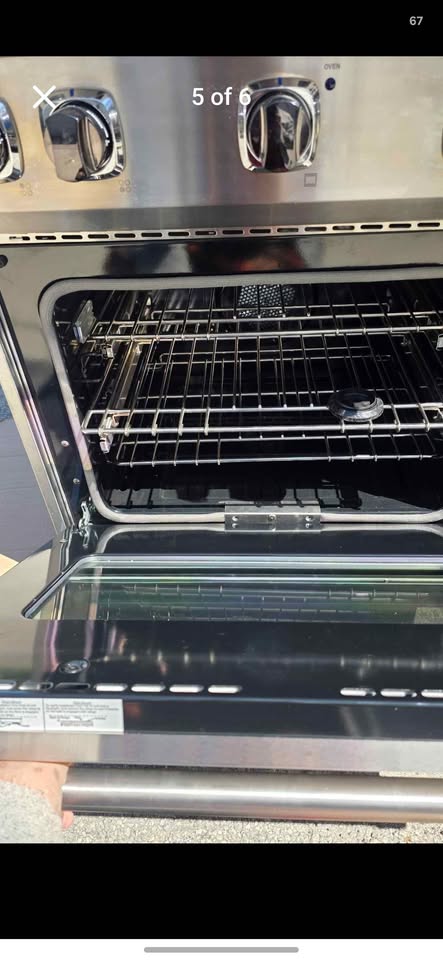 A stainless steel freestanding oven with the door open, showing interior racks and a glass door. Control knobs are visible along the top edge.